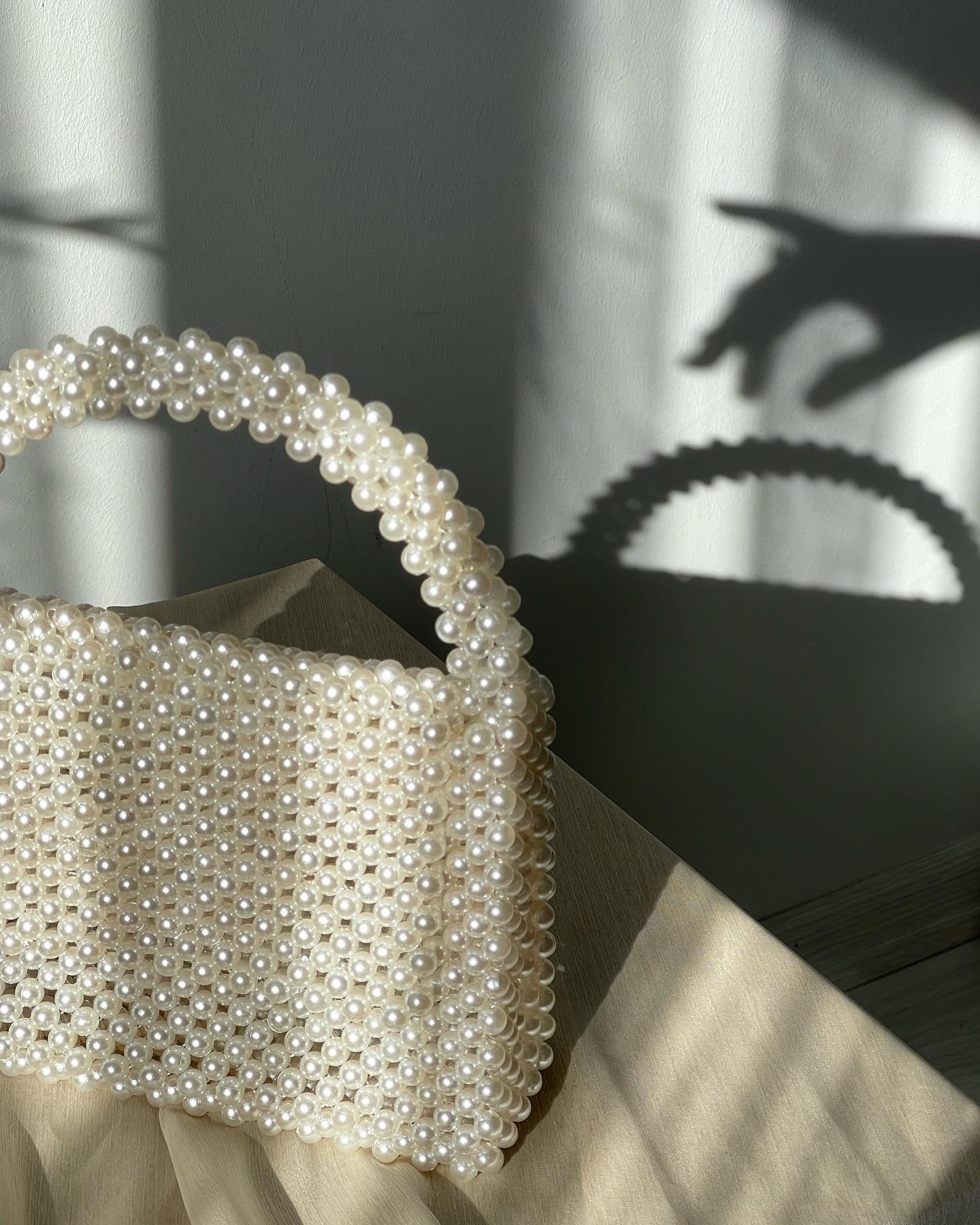 May include: A white beaded handbag with a top handle. The bag is made of small, round pearls and has a rectangular shape.